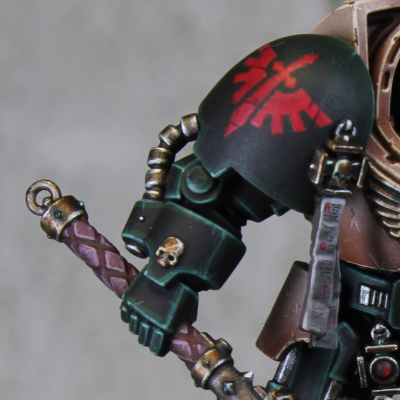 Close view of a dark green shoulder with fine green edge highlights and a red chapter symbol